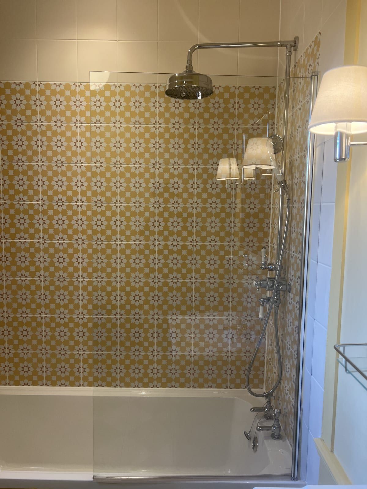 Period-style bathroom with yellow patterned tiles, a brass rain shower and wall lights