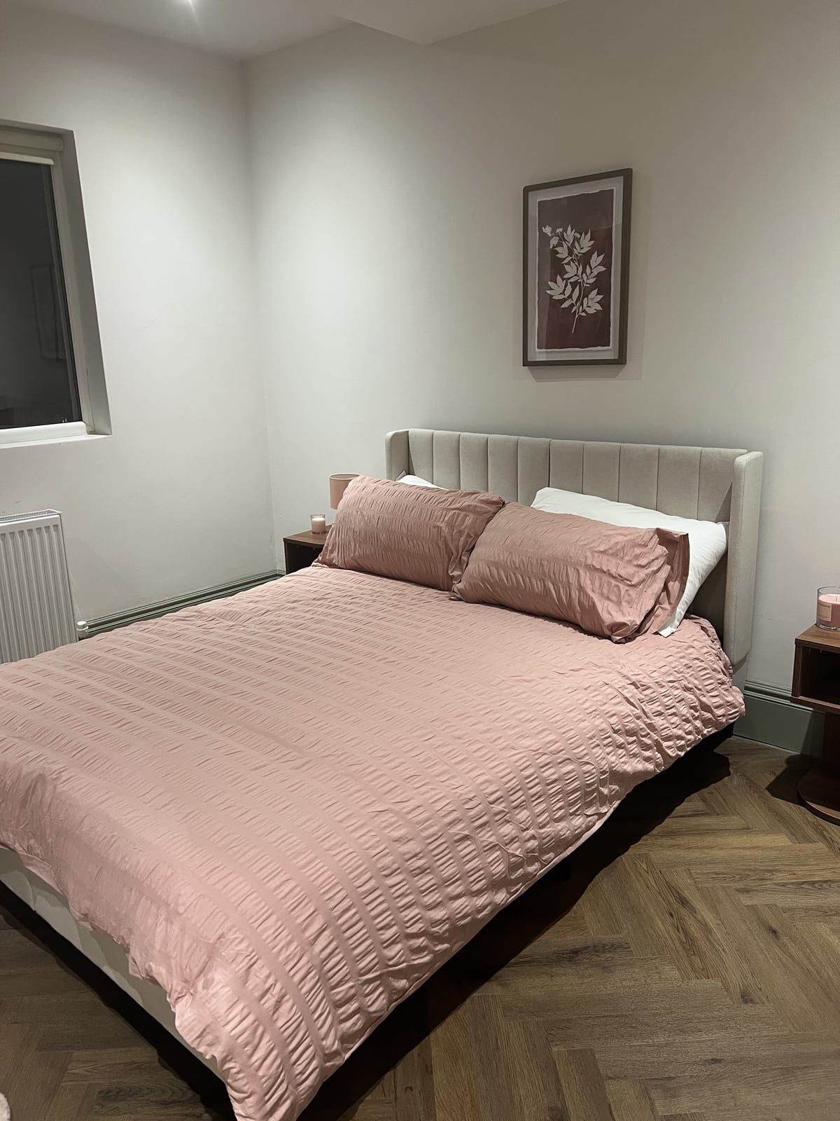 Bedroom with a made-up double bed in pink bedding on a herringbone floor
