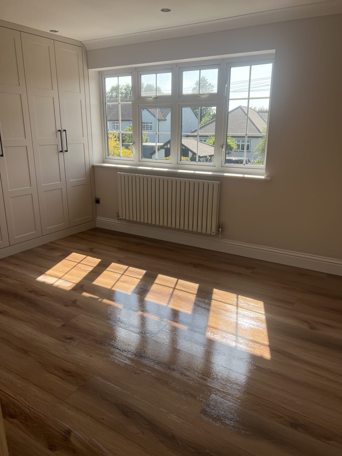 Empty bedroom with sunlight across a polished wooden floor and built-in wardrobes