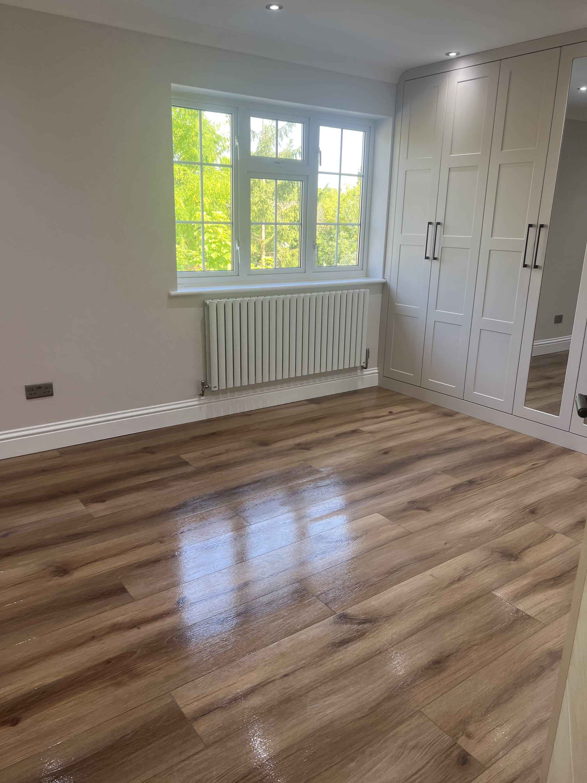 Empty bedroom with a polished wooden floor, white fitted wardrobes and a radiator under the window