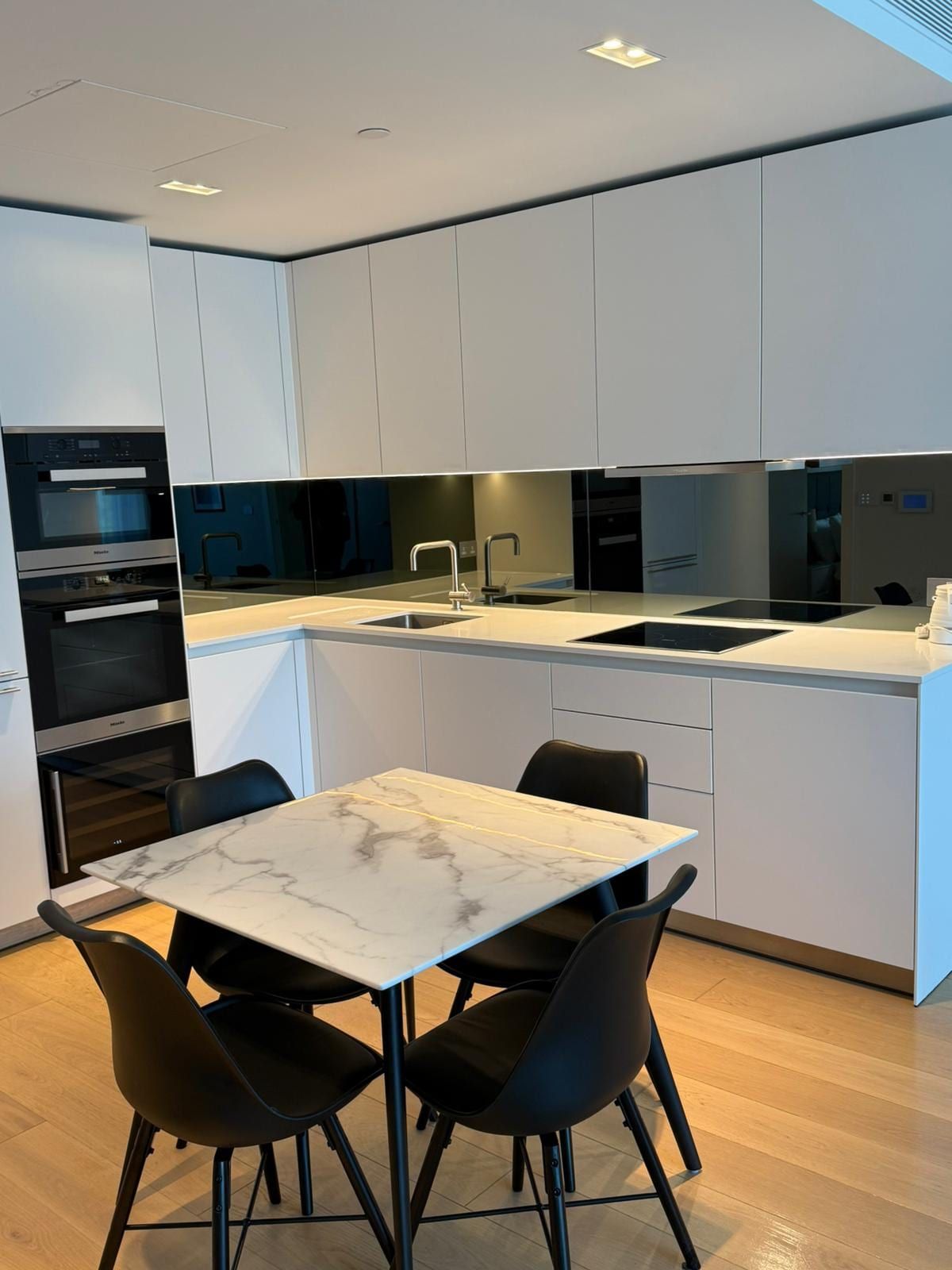 Modern white kitchen with black glass splashback and a marble-topped dining table