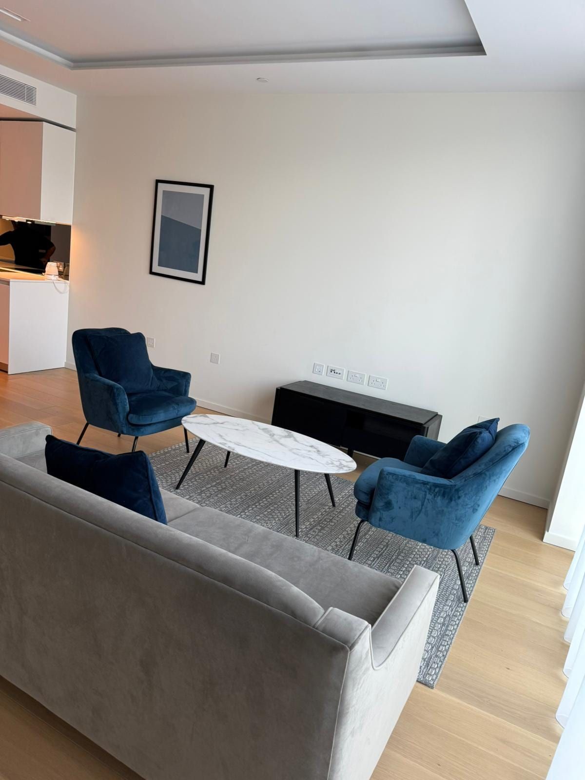 Flat living room with a grey sofa, two blue velvet armchairs and a marble coffee table