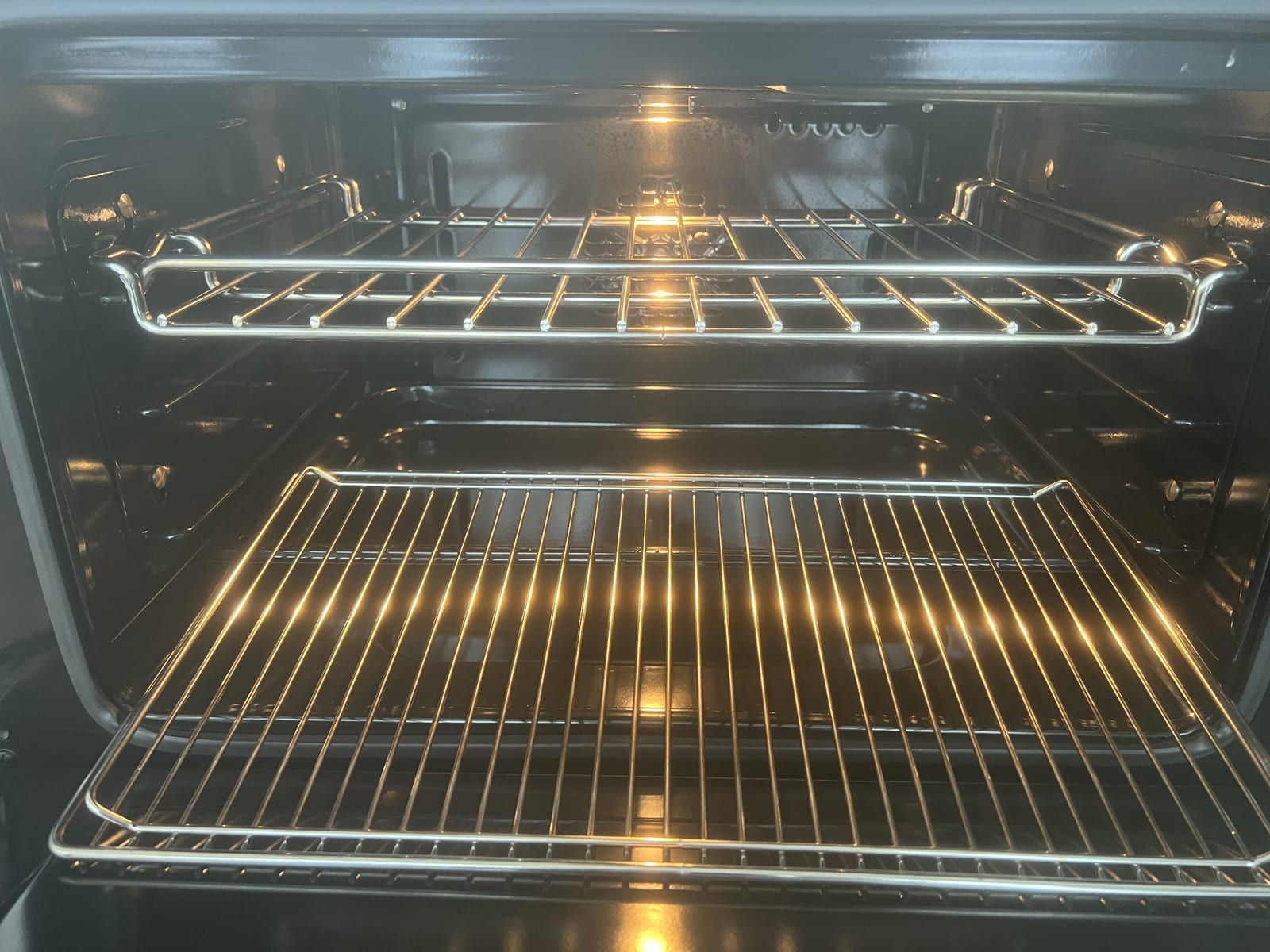 Inside a clean oven with the light on, showing the enamel and two chrome shelves