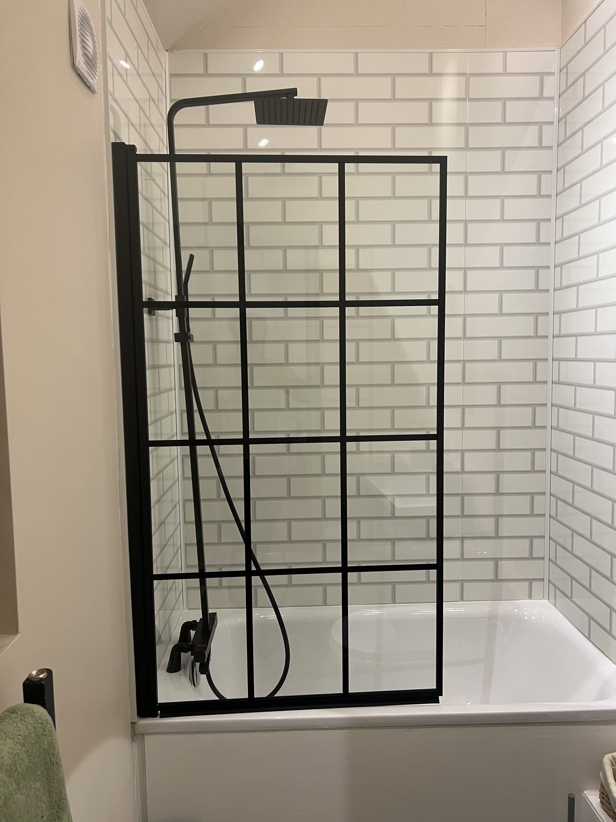 Shower over a bath with a black grid glass screen and white metro tiles