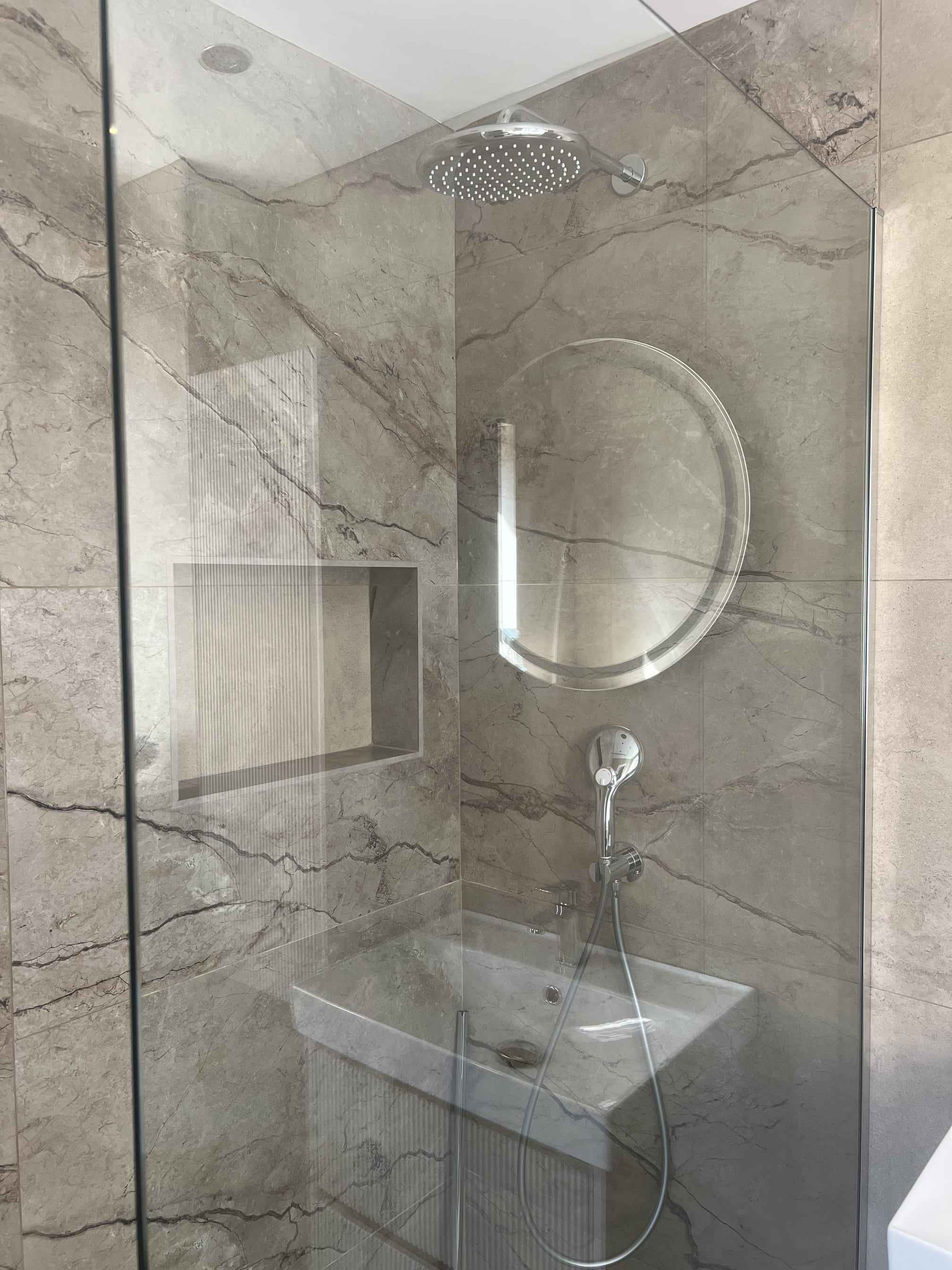 Walk-in shower with grey marble-effect tiles, a round mirror and a tiled niche